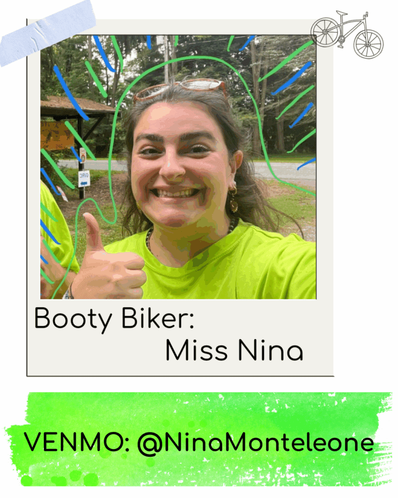 Smiling woman in green shirt gives thumbs up outdoors.