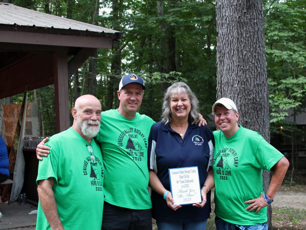 Four people at camp, person holds appreciation plaque.