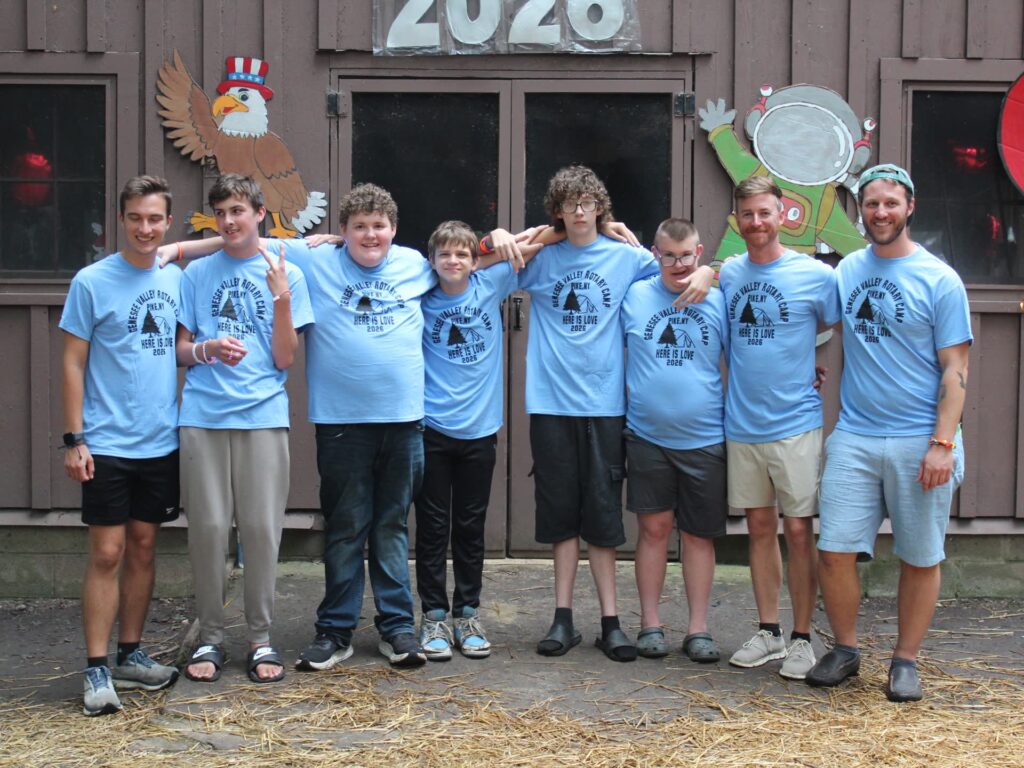 Seven people in matching camp shirts pose outside cabin